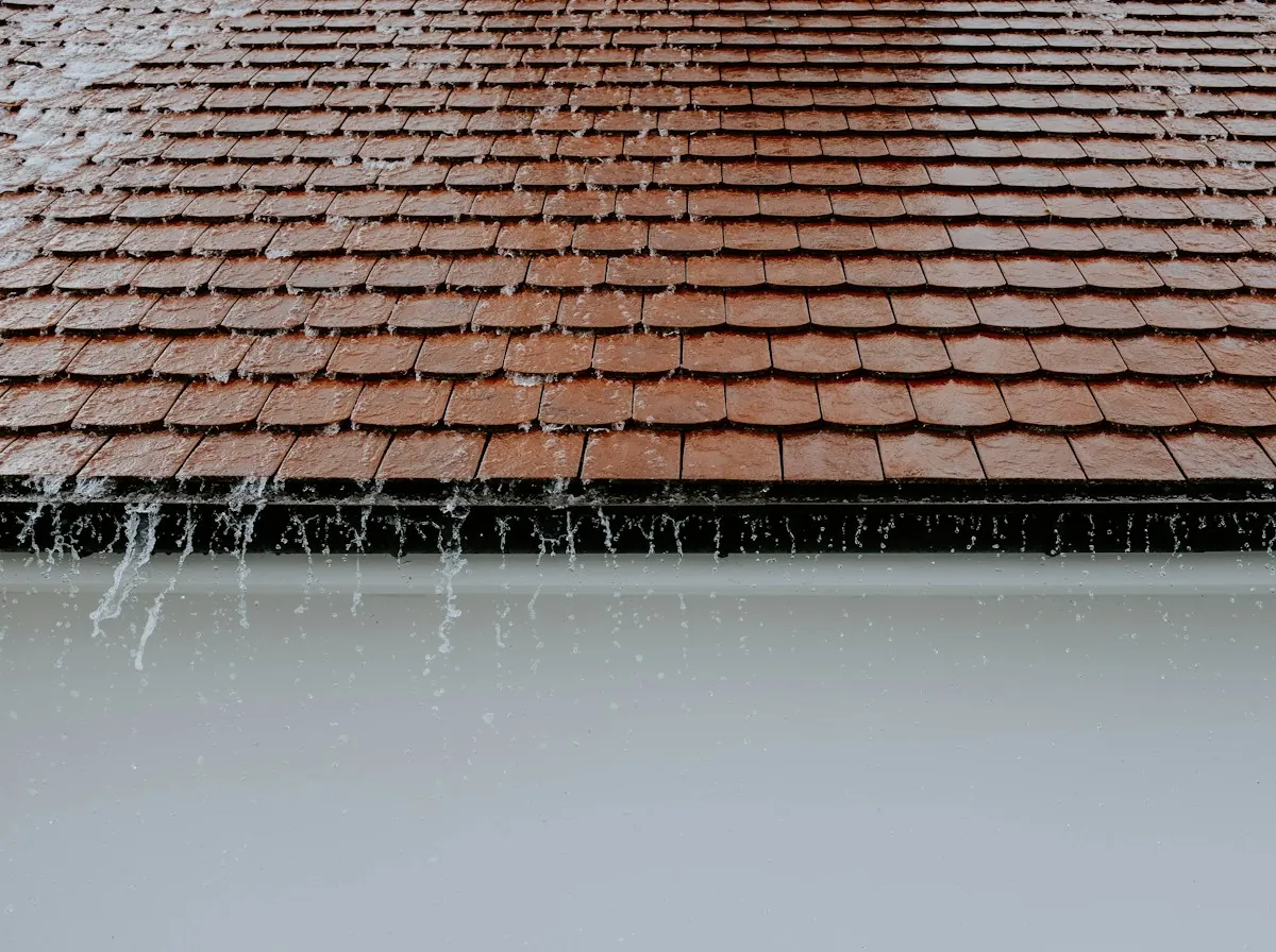 Flat Roof Replacement in Sherman — rain dripping from the edge of a tile roof
